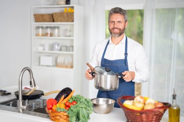 Şef mutfakta sebze pişiriyor. Önlüklü bir adam hammaddeyle sağlıklı bir yemek hazırlar. Sebzeli yemek. Akşam yemeği için taze sebzeli şef. Aşçı sebzelerle kahvaltı hazırlar.