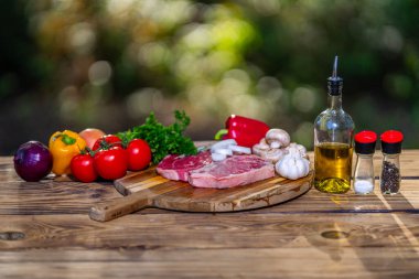Raw beef steak on wooden board with ingredients. Fresh sliced meat prepared for cooking. Beef fillet with rosemary and pepper. Raw beefsteak. Fresh meat slice ready for grill or barbecue