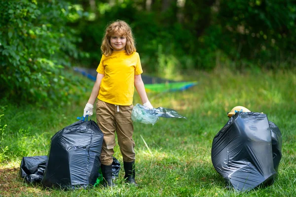 Çöp poşeti dolusu çöp ve çöp maşası olan bir çocuk. Geri dönüşüm kutusuyla ormanda veya parkta plastik atık toplayan sevimli bir çocuk. Çevre aktivistleri. Çevresel koruma ve ekoloji