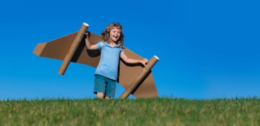 Dışarıda oyuncak jetpack 'i olan bir çocuk. Yeşil yay tarlasında karton kanatlarla oynayan bir çocuk. Bahar yolculuğu ve macera