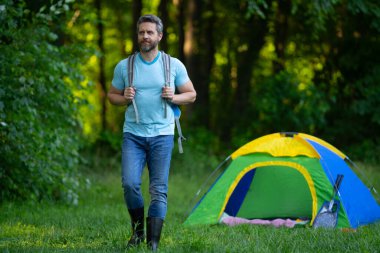Gezgin doğada kamp yapmaktan hoşlanıyor. Doğaya yaz gezisi. Orman kampında dinlenen adam. Kamp gezisi. Yürüyüşten sonra çadırın yanında dinleniyor. Barışçıl bir kamp alanında özgürlük tatili. Yazın piknikteki adam
