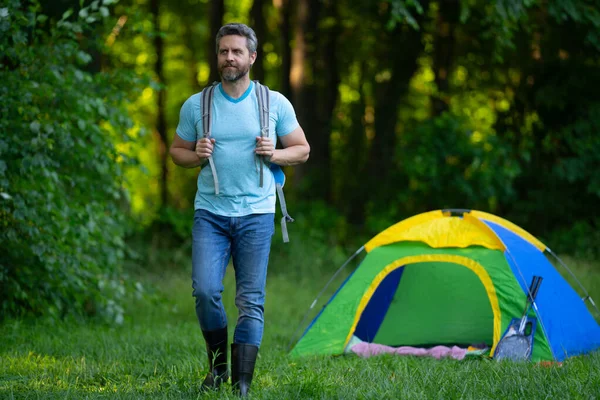 Gezgin doğada kamp yapmaktan hoşlanıyor. Doğaya yaz gezisi. Orman kampında dinlenen adam. Kamp gezisi. Yürüyüşten sonra çadırın yanında dinleniyor. Barışçıl bir kamp alanında özgürlük tatili. Yazın piknikteki adam