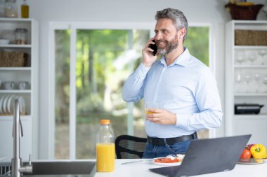 Orta yaşlı adam bir sabah kahvaltısını mutfakta yer. Adam sabah mutfağında sağlıklı bir yemek için sebze yiyor. Adam mutfakta sağlıklı yiyecekler yiyor. Modern mutfakta sabah kahvaltısı.