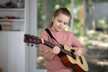 Çocuk evde akustik gitar çalıyor. Çocuk oturma odasında gitar çalışıyor. Genç gitarist içeride müzik öğreniyor. Müzik dersi sırasında gitar çalan bir çocuk. Çocuk odada gitar çalıyor.