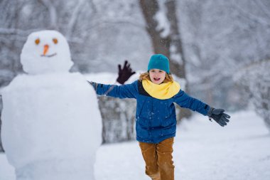 Çocuk kışın kardanadamla oynuyor. Kış günü havuç burunlu bir kardan adam. Kardan adam yapan çocuk. Karlı kış parkında komik kardan adam için kartopu yapan küçük çocuk. Karlı kış parkında kardan adamlar