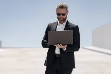 İş adamı dışarıda dizüstü bilgisayar kullanıyor. Dizüstü bilgisayar kullanan başarılı bir adam. Dizüstü bilgisayarı olan kendine güvenen bir iş adamı. İnternette iş. İş adamı laptoptaki verileri kontrol ediyor. Takım elbiseli iş adamı internette çalışıyor.