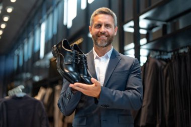 Takım elbiseli şık bir adam bir butikte lüks ayakkabılara hayran. Bir iş adamı bir ayakkabı mağazasında şık ayakkabılar seçer. Resmi görünmek için klasik deri ayakkabılar. Resmi ayakkabılar