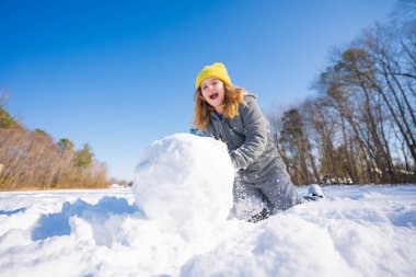 Oyuncu çocuk karda kış eğlencesinin tadını çıkarıyor. Kardan adam yapan çocuk. Kartopu yapan çocuk. Çocuk kardan adam için kartopu yapıyor. Dışarıda kış oyunu oynayan gülümseyen bir çocuk. Kar oyunundan hoşlanan çocuk