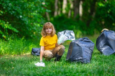 Lastik eldivenli çocuk çöp torbasıyla ormandaki çöpleri temizliyor. Eko, çevre koruma. Kirliliği geri dönüştür. Çocuk çöp ve plastik çöp topluyor. Çevreyi koru. Eko çocuklar
