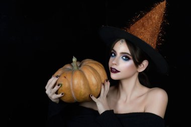 Halloween banner. Beauty girl holding pumpkin. Young woman witch posing in studio. Witchcraft theme with woman with witch Halloween hat. Halloween portrait of witch. Girl with Halloween makeup