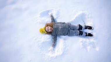 Mutlu bir çocuk için eğlenceli bir kış günü. Kar meleği kışın neşeli bir çocuk tarafından yapılmış. Karda uzanmış rahat elbiseli bir çocuk. Tatlı çocuk kar melekleri yapıyor. Kış eğlencesi Neşeli kış anı