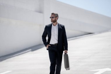 Açık hava iş portresi. Dışarıda yürüyen bir iş adamı. Başarılı lider hareket halinde. Çantalı takım elbiseli adam. İşadamı işe gidiyor. Çantası olan bir iş adamı. İş başarısı