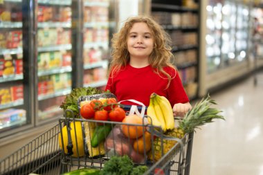 Süpermarkette el arabasıyla çocuk alışverişi. Çocuk markette taze sebze seçiyor. Yiyecek satan bir çocuk. Markette ürün seçen bir çocuk. Bakkalda taze yiyeceği olan çocuk