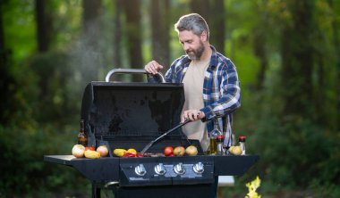 Arka bahçede barbekü yapan bir adam. Orta yaşlı erkek şef ızgara terasında gurme eti pişiriyor. Açık hava ızgarası. Arka bahçedeki ızgarada ızgara et. Izgara barbekü bbq konsepti