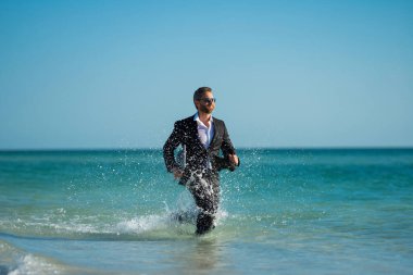 Denizde takım elbiseli komik bir iş adamı. Yaz tatili, deniz sahilinde iş. Yaz tatili, iş adamları konsepti. İş adamı uzaktan kumandası çalışıyor. Yaz tatilleri için ofis çalışanları hayal edin.