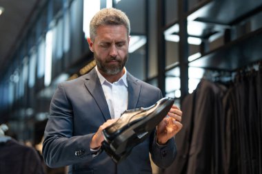 Takım elbiseli adam butikte lüks ayakkabılara bayılır. Bir iş adamı bir ayakkabı mağazasında şık ayakkabılar seçer. Resmi görünmek için klasik deri ayakkabılar. Resmi ayakkabılar. Deri ayakkabılar.