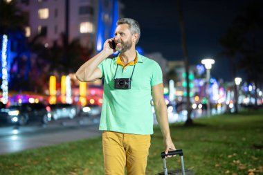 Gece sokağında telefonla konuşan bir adam. Gece yarısı bir turist arıyor. İspanyol adam telefon kullanıyor. Seyahat sırasında telefonla konuşan olgun bir adam. Cep telefonu olan, tişörtlü, yakışıklı, olgun bir adam.