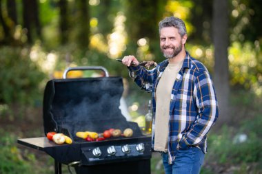 Arka bahçede barbekü yapan bir adam. Şef 40 'lı yaşlarda dışarıda ızgara terasında gurme eti pişiriyor. Açık hava ızgarası. Arka bahçedeki ızgarada ızgara et. Izgara barbekü bbq konsepti