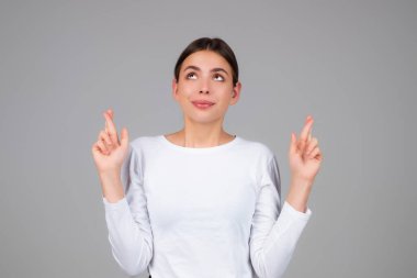 Olumlu ifadeli genç bir kadın şans diliyor. Rüya umutları, dilekler, gri arka planda izole edilmiş. Umut dolu bir kadının portresi, davranış tepkisi. Kız şans diliyor.