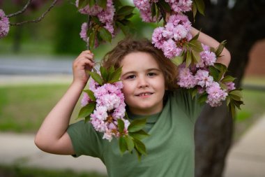Çocuğun etrafında bahar çiçekleri var. Çiçek açan bahçede bir çocuk. Çiçeklere yakın bir çocuk yüzü. Hayalperest çocuk portresi. Açık havada çocuklar çiçek açan ağaçlarla portre yaparlar. Çocuğa ve çiçeklere yakın çekim