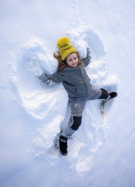 Mutlu çocuk kışın bir kar meleği yapıyor. Dışarıda karda oynayan bir çocuk. Karda yatan çocuk melek kanatları yapıyor. Melek çocuk kışın oynar. Kar melekleri yapan mutlu bir çocukla kış eğlencesi