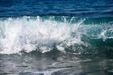 Deniz dalgalarının arka planında gün ışığı. Okyanus dalgaları güneş ışığında kırılır ve parlar. Mavi deniz dalgaları yaz parlaklığında parıldıyor. Dalgalar sıçrıyor. Deniz dalgaları bir okyanus dokusu