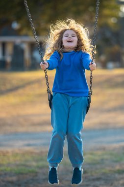 Bahar parkında sallanan neşeli çocuk. Sarı saçlı küçük bir çocuk salıncakta sallanıyor. Parkta gülümseyen mutlu çocuk. Mutlu çocukluk anları. Çocuk dışarıda oynuyor. Çocuk salıncakta eğleniyor. Çocuklar için açık hava oyunu