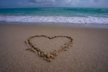 Kalp kumda çizilmiş. Dalgalar kalp şeklinde bir işaret oluşturuyor. Kumsalda aşk. Romantik yaz. Kumdan yapılmış bir kalp. Aşk ve okyanus dalgaları