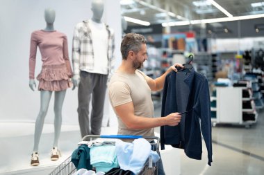 Olgun adam şık kıyafetler alıyor. Tüketici yeni kıyafet bölümünü inceliyor. Şık bir müşteri şık bir kot pantolon dener. Bir erkek alışverişçi moda kıyafetler satın alır. Bir erkek moda kıyafetlerini seçer