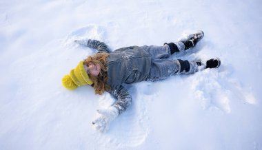 Mutlu çocuk kış günü kar meleği yapıyor. Dışarıda karda yatan gülümseyen çocuk. Çocuk soğuk kış havasının tadını çıkarıyor. Dışarıda karda oynayan neşeli bir çocuk. Çocuk karda eğleniyor.
