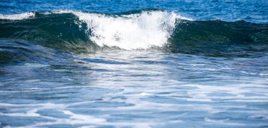 Okyanus dalgaları beyaz köpük oluşturuyor. Parlak güneş ışığı hareket halindeki okyanus dalgalarını yansıtır. Deniz dalgaları sahilde yuvarlanıyor. Güçlü deniz dalgaları köpüklü spreyle yükselir. Dalga dokusu