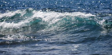 Parlayan deniz dalgaları gün ışığında parıldıyor. Okyanus dalgası yükseliyor. Parlak deniz dalgaları arka planı. Okyanus dalgaları sahilde yuvarlanıyor. Mavi yeşil deniz dalgaları deseni