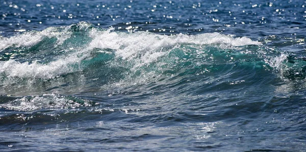 Parlayan deniz dalgaları gün ışığında parıldıyor. Okyanus dalgası yükseliyor. Parlak deniz dalgaları arka planı. Okyanus dalgaları sahilde yuvarlanıyor. Mavi yeşil deniz dalgaları deseni