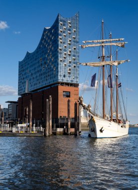 Hamburg 'daki Elbe Nehri' nin kültürel simgesi. Güneşli havada şehrin ufuk çizgisi ve limanı. Yakınında yelkenli teknesi olan ünlü modern konser salonu. Hamburg, Elbe Filarmoni Salonu