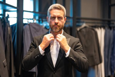 Bir adam butikte alışveriş yaparken klasik bir terzi kıyafeti giyer. Başarılı bir iş adamı için klasik bir kıyafet. Takım elbiseli modaya uygun bir mağaza. Olgun bir adam bir takım elbise seçer. Bir erkek resmi etkinlik için takım elbise seçer.