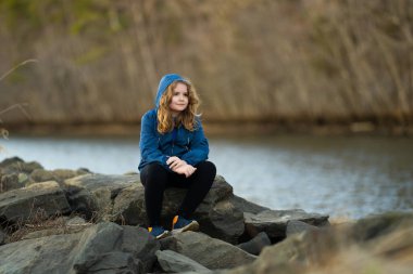 Çocuk nehir kıyısındaki bir rıhtımda yürüyor. Çocuk nehir kıyısında kayalıklarda yürüyor. Çocuk açık havada düşünceli. Doğada sıradan bir genç. Sakin ve sessiz çocuk nehirde dinleniyor. Sonbahar parkında temiz hava alan çocuk.