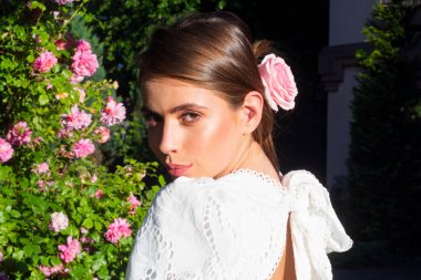 Bahar havası. Genç, zarif moda hanımı beyaz yaz elbisesi pembe bahar çiçekli gül bahçesinde poz veriyor. Portreyi kapat