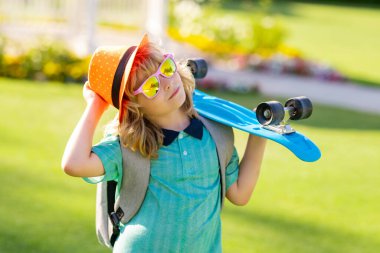Güneş gözlüklü, moda şapkalı, dışarıda kaykayla poz veren mutlu bir çocuk. Aktivite ve mutlu çocukluk kavramı