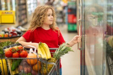 Sepetli çocuk sebze reyonunda. Çocuk markette meyve topluyor. Alışveriş arabalı çocuk. Çocuk süpermarkette alışveriş yapıyor. Çocuk sağlıklı ürünler alıyor. Marketteki çocuk