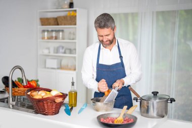 Mutfakta sebze doğruyor. Önlüklü aşçı modern mutfakta sağlıklı yemek hazırlar. Mutfakta sebzeli yemek. Aşçı evde sebzelerle kahvaltı hazırlar.