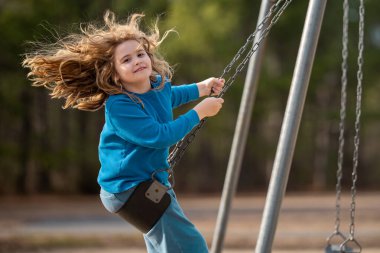 Dışarıda sallanan mutlu çocuk. Salıncakta gülen çocuk. Oyun bahçesinde oynayan neşeli çocuk. Heyecanlı çocuk salıncakta sallanıyor. Yaz parkındaki sevimli çocuk. Parkta sallanan oyuncu çocuk. Mutlu çocukluk
