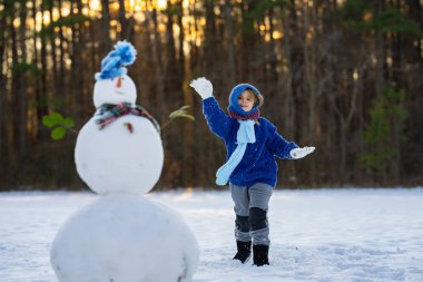 Çocuk dışarı kar fırlatıyor. Karlı parkta oynayan bir çocuk. Karda mutlu çocuk yüzü. Küçük çocuklar için kış eğlencesi. Kış şapkalı çocuk gülümsüyor. Çocuklar kışın tadını çıkarıyor. Çocuk dışarıda kartopu oynuyor.