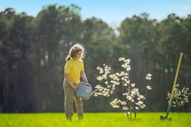 Bahçede çalışan bir çocuk. Çevre için büyüyen ağaç ve bakım bitkisi. Ekim mevsimi. Bitki yetiştiren bir çocuk. Bahçe işleri. Meyve sulayan çocuk. Çocuk dikme ağacı. Bahar günü
