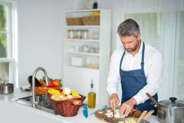 Mutfakta sebze doğruyor. Önlüklü şef modern mutfakta sağlıklı yemek hazırlıyor. Mutfakta sebzeli yemek. Aşçı evde sebzelerle kahvaltı hazırlar.