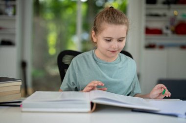 Evde kitap okuyan sevimli bir çocuk. Akıllı çocuk ders kitaplarıyla çalışıyor. Öğrenci, rahat bir odada kitap ödevi okuyor. Öğrenci çocuk kitap okumaya odaklandı. Sınıfta masal okuyan zeki çocuk.