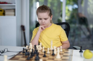 Çocuk evde satranç oynuyor. Çocuk satranç hamlesini düşünüyor. Çocuklar satrançla strateji öğrenir. Çocuk satranç tahtasına konsantre oluyor. Gençler satranç oynuyor. Masada oyun oynayan düşünceli bir çocuk.