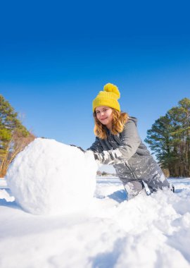 Güneşli bir kış gününde büyük bir kartopu yuvarlayan mutlu çocuk. Dışarıda karda oynayan gülümseyen çocuk. Kar topu yaparken kışın eğlenen tatlı bir çocuk. Neşeli çocuk taze karda kardan adam yapıyor.