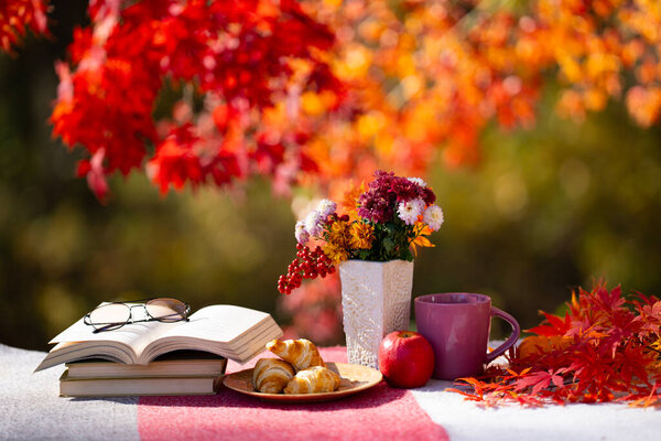 Cozy autumn background. Vase of autumn flowers. Cozy autumn rest. Sweet pastries book and leaves on table. A calm autumnal scene. The warm autumn day