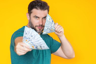 İyi ödeme. Yakışıklı adam gri stüdyoda izole edilmiş para tutuyor. Dolar banknotları halinde para. Yığınla para, finans, yatırım ve tasarruf
