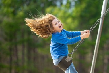 Çocuk parkta salıncakta sallanıyor. Sarı saçlı küçük bir çocuk salıncakta sallanıyor. Salıncakta gülümseyen mutlu çocuk. Mutlu çocukluk anları. Çocuk dışarıda oynuyor. Çocuk salıncakta eğleniyor. Çocuklar için açık hava oyunu